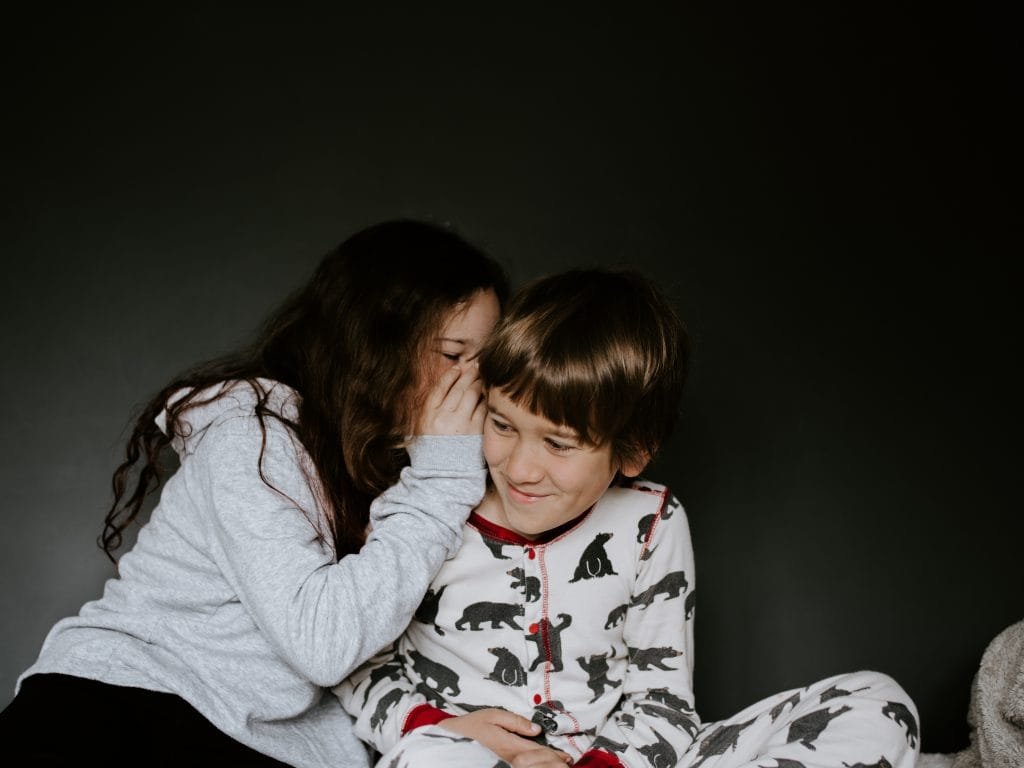 Description: girl in gray jacket whispering on boy's right ear